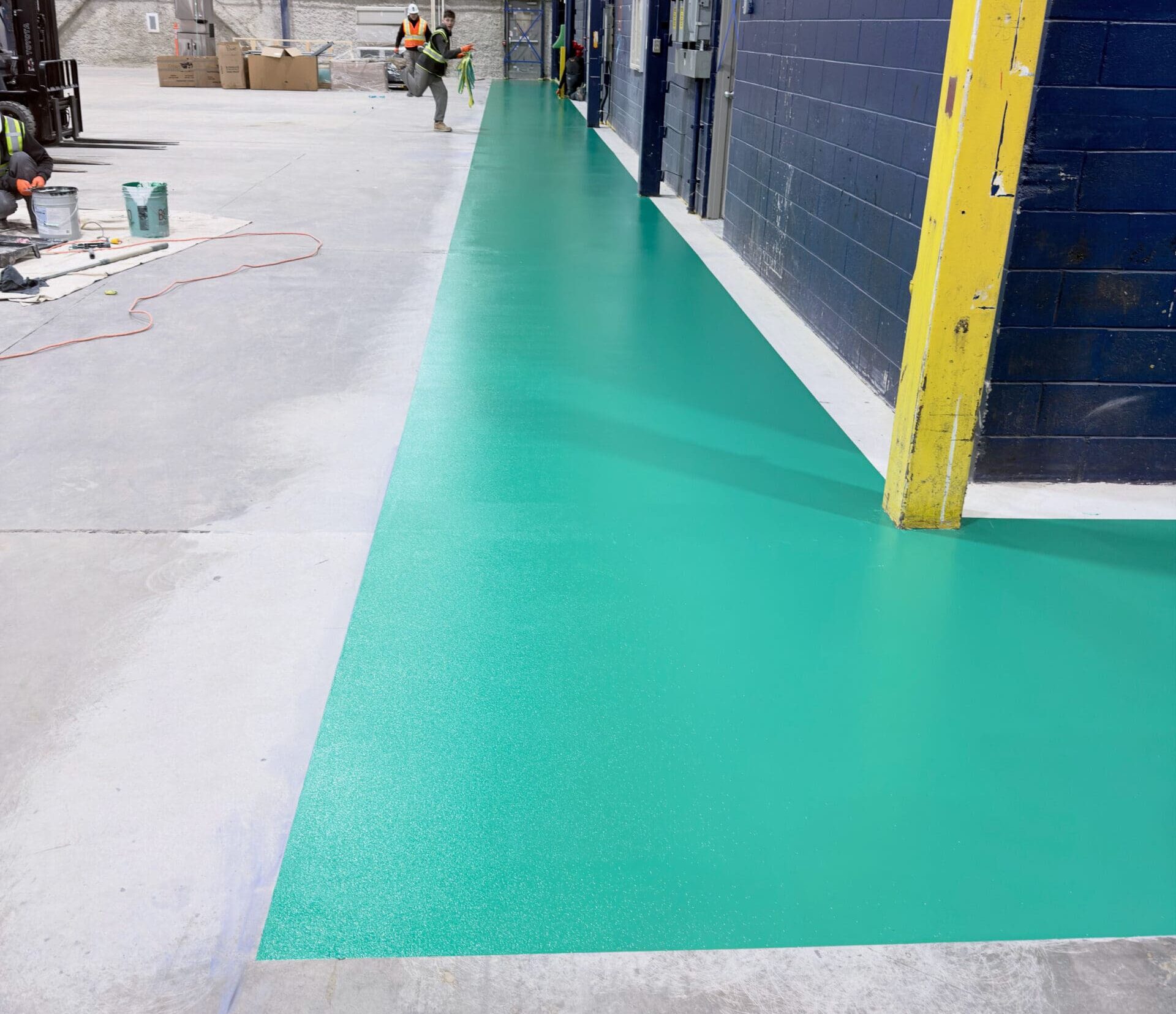 Green epoxy-coated industrial walkway with anti-slip finish installed on concrete floor inside warehouse, creating a clearly defined pedestrian path alongside workstations.