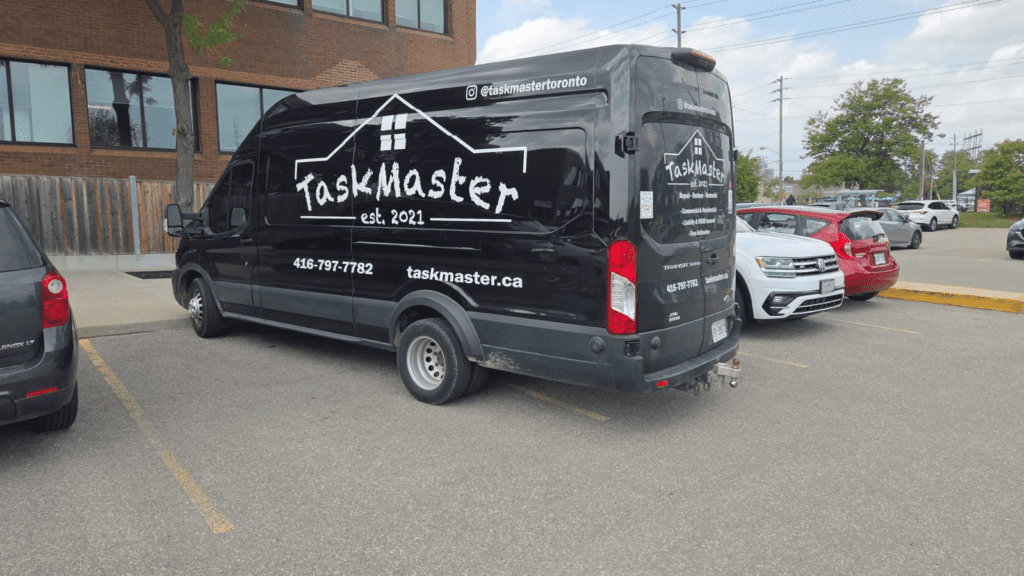 Black TaskMaster service van parked outside a commercial building in Mississauga, displaying the TaskMaster logo, website, and phone number.